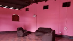 Ein Zimmer mit rosafarbenen Wänden, zwei schwarzen Sofas, einem kleinen Rundbogenfenster und einem gefliesten Boden.