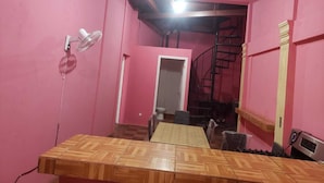 Ein Zimmer mit einem Holzespeise Tisch, rosa Wänden, einem Deckenventilator, einer Treppe und einer Tür zu einem anderen Raum.