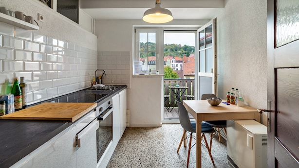 Une cuisine avec un plan de travail en bois, une table à manger avec des chaises, un réfrigérateur et une vue sur les bâtiments par une fenêtre.