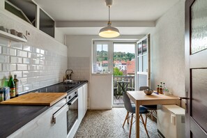 A kitchen with a wooden countertop, a dining table with chairs, a refrigerator, and a view of buildings through a window.
