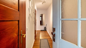 Un couloir avec des portes en bois, un luminaire, un tapis et une vue sur une autre pièce.