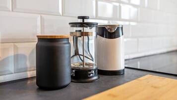 A kitchen counter with a coffee maker, a grinder, and a thermos.