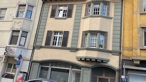 Un immeuble à plusieurs étages, de style architectural classique, qui se distingue par une grande baie vitrée, de nombreux balcons et une entrée située au niveau du rez-de-chaussée.