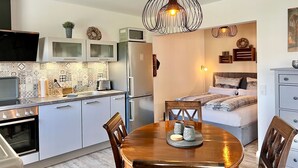 A compact kitchen with modern appliances, a dining table with chairs, and a bedroom with a bed and bedside tables. - fewo1846 - UferNest (App. 603) / Studio apartment with balcony on the 1st floor - (Harrislee)