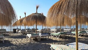 Ein Strand mit Liegestühlen und Sonnenschirmen aus Palmblatt, die Schatten spenden.