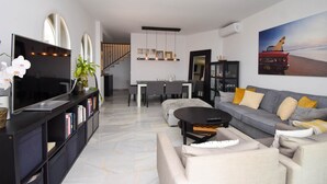 Un soggiorno moderno con una TV a schermo piatto, un'area pranzo con tavolo e sedie, e un divano grigio con cuscini gialli.