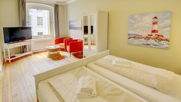 Une chambre d’hôtel avec un lit, une télévision, un fauteuil rouge et un tableau représentant un phare.