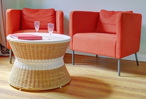 A wicker table with two glasses and a pink notebook, flanked by two orange armchairs.