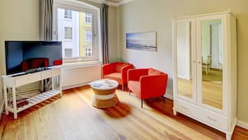 Un salon moderne avec une télévision, des fauteuils rouges, une table basse en osier et une grande armoire.