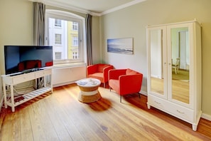 A modern living room with a television, red chairs, a wicker coffee table, and a large wardrobe.