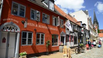 Un bâtiment rouge portant l’enseigne « BRAASCH-HOF WEIN & RUMHAUS BRAASCH » et un drapeau blanc avec le texte « Unss braa ».