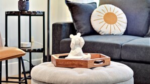 Un soggiorno moderno con un divano grigio, un tavolino in legno e una scultura bianca decorativa su un pouf.