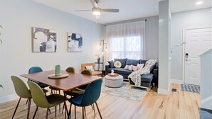 Un soggiorno moderno con un tavolo da pranzo in legno, sedie verdi e blu, un divano grigio e una ventola a soffitto.