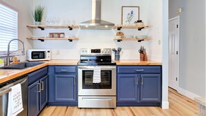 Una cucina moderna con pensili blu scuro, un piano cottura in acciaio inossidabile, un forno a microonde ed scaffali in legno sopra il bancone.