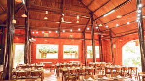Een restaurant met meerdere eettafels, houten stoelen en een hoge plafond met zichtbare balken.