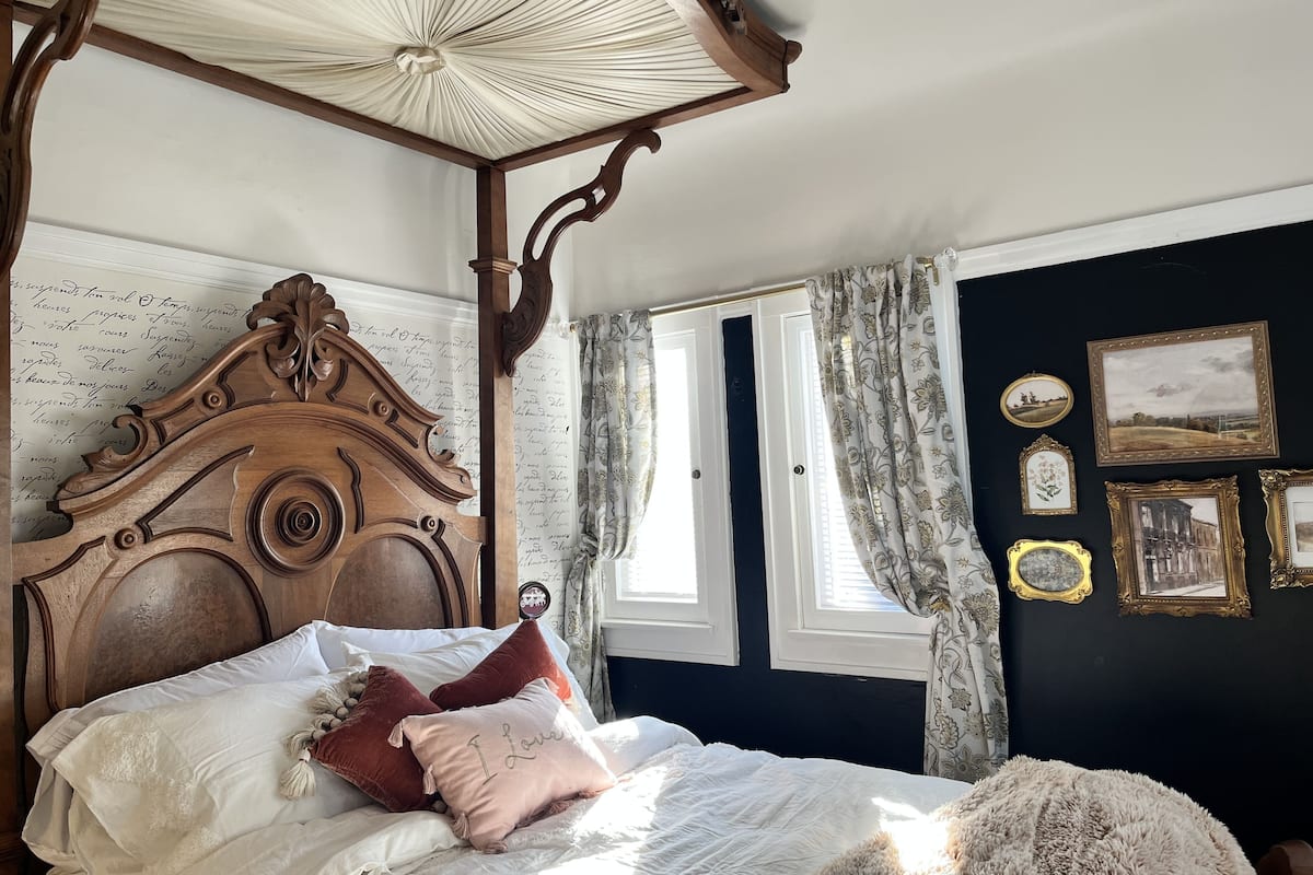 Un dormitorio con cama con dosel, dosel y ventana con cortinas.