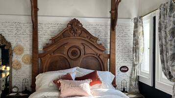 A four-poster canopy bed with a floral-patterned headboard, a fluffy rug, and a nightstand with a clock and a small lamp.
