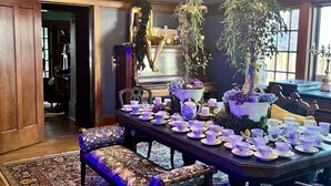 Un comedor con una mesa dispuesta para el té, rodeada de sillas con tapicería floral, una araña y un techo estampado.