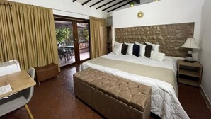 Habitación de hotel con una cama grande, un escritorio y un balcón con cortinas.