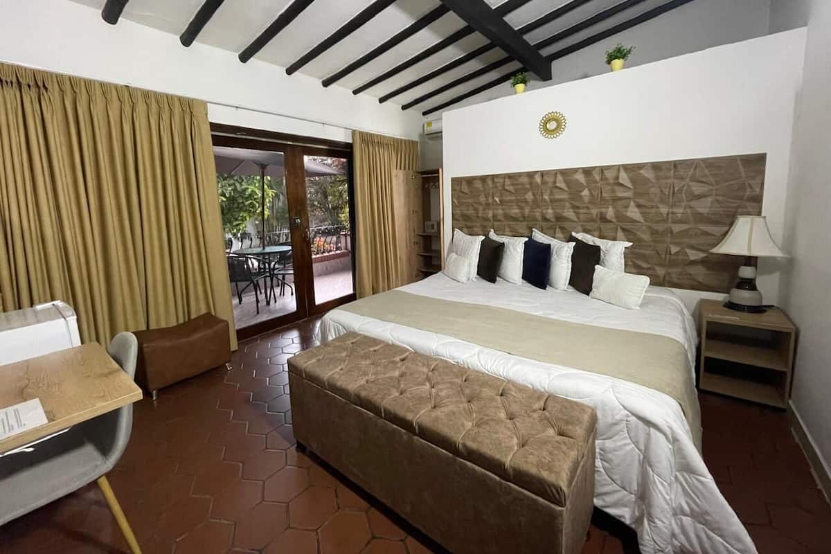 Habitación de hotel con una cama grande, un escritorio y un balcón con cortinas.
