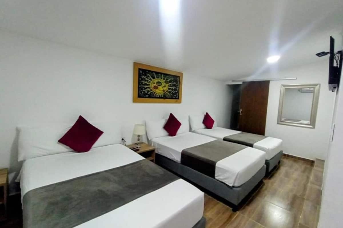 A hotel room with three beds, a painting on the wall, a wooden floor, and a door.