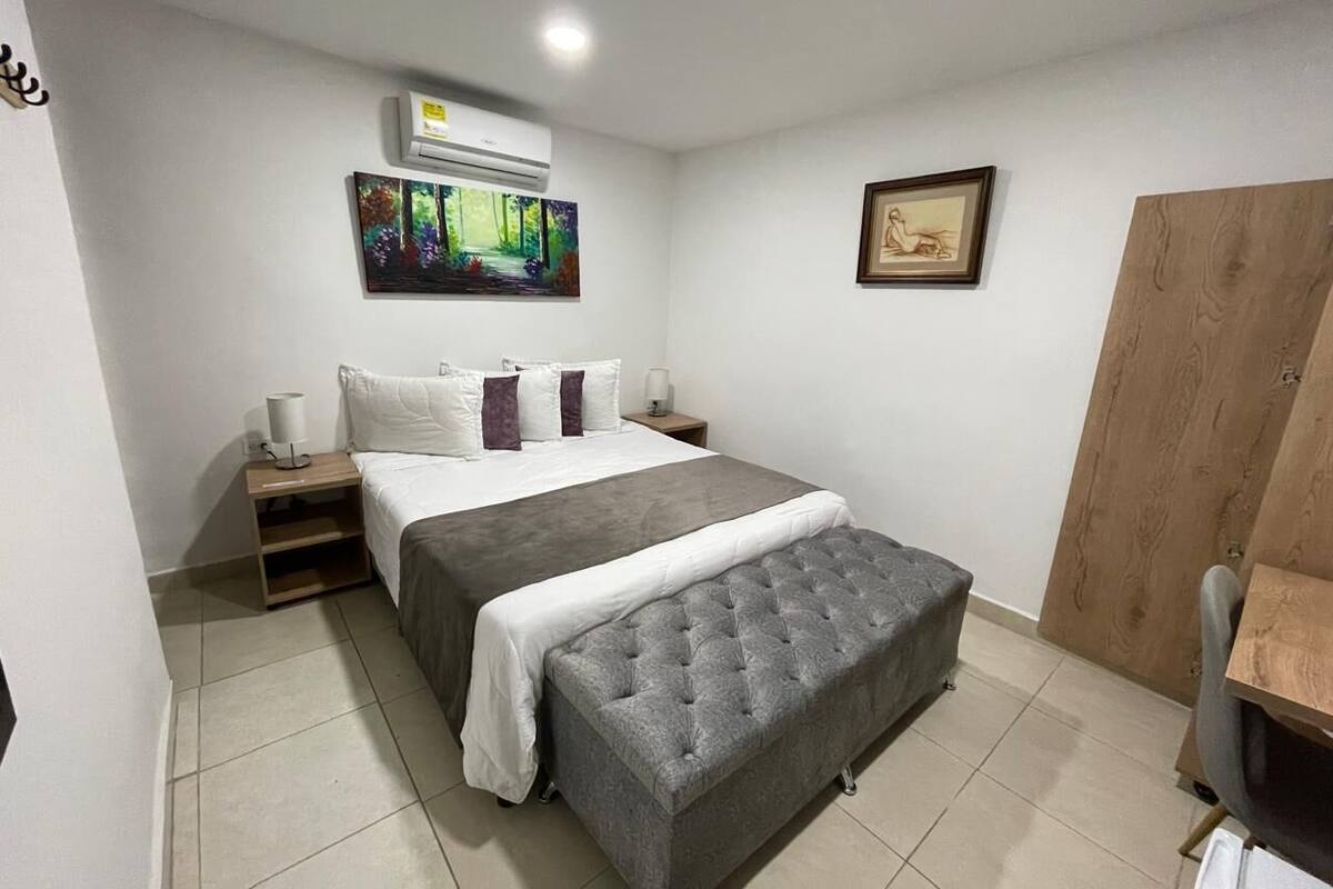 A bedroom with a bed, bedside tables, a bench, a wardrobe, and a painting on the wall.