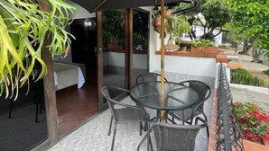Un patio exterior con una mesa, sillas, un paraguas grande y plantas en macetas.
