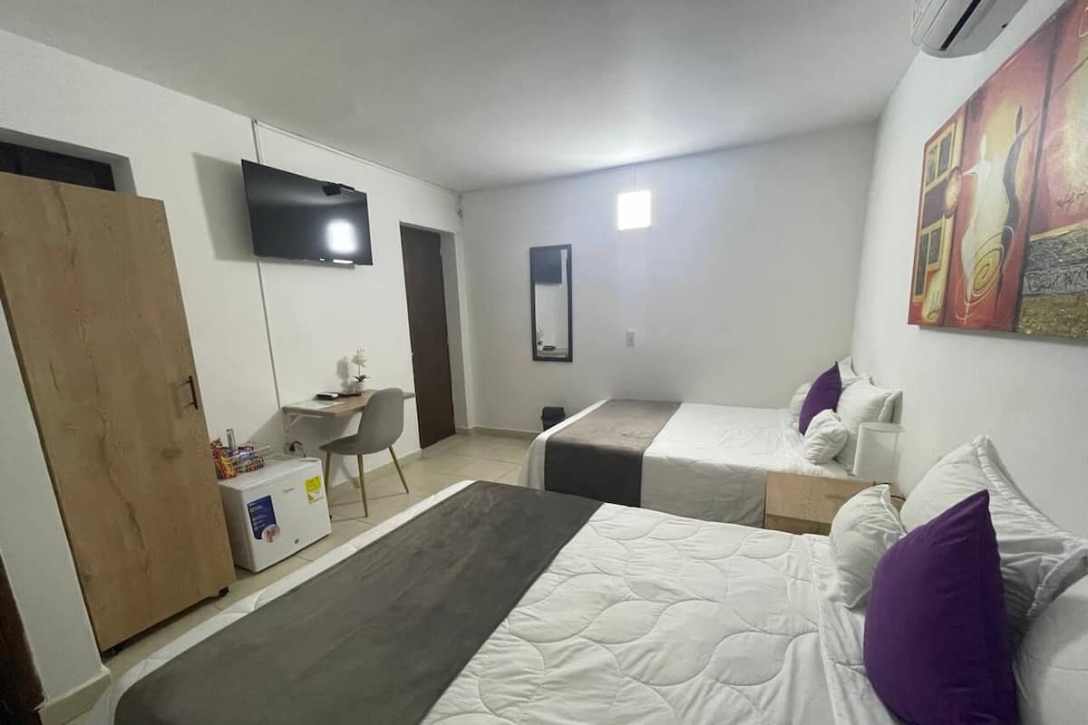 A hotel room with two beds, a desk, a chair, a TV, and a painting on the wall.