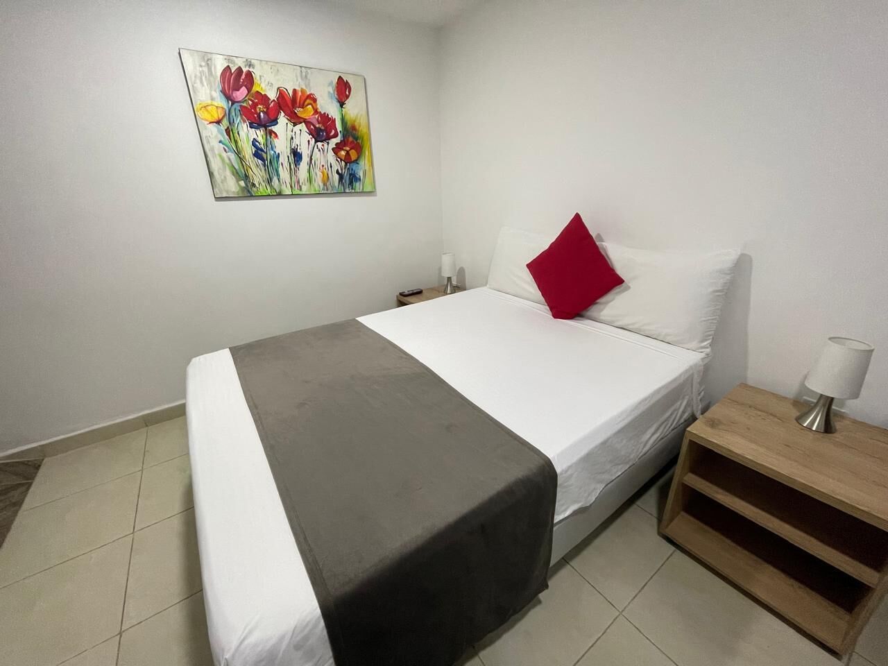 Un dormitorio con cama, mesita de noche, lámpara y un cuadro en la pared.
