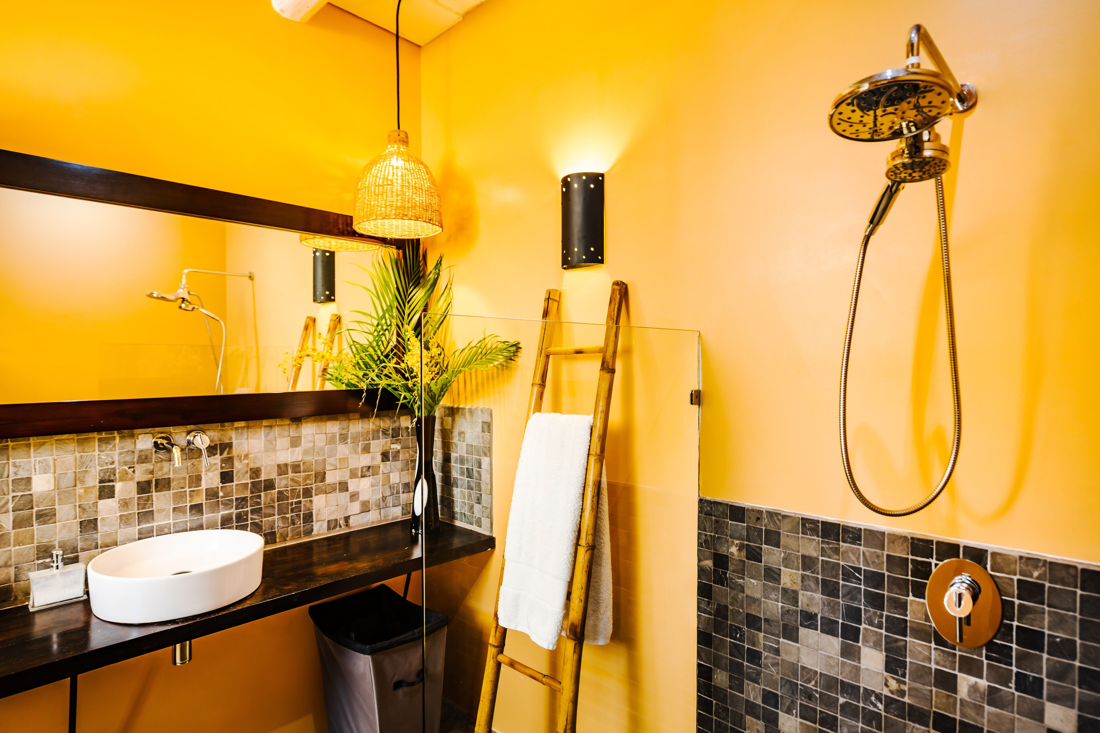 Une salle de bain avec un lavabo rond, un porte-serviettes, une pomme de douche et un mur recouvert de mosaïques.