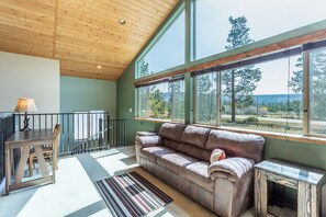 A cozy room with a wooden ceiling, large windows, a sofa, a dining table, and a lamp. - Beautiful retreat on Hat Creek, Fire pits, Fishing and  15 min. from Lassen Park (Old Station)