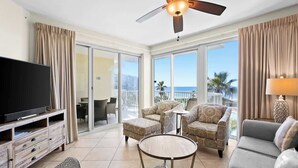 Ein geräumiges Wohnzimmer mit Flachbildfernseher, Deckenventilator und Balkon mit Meerblick.
