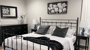 A bedroom with a bed, a dresser, a nightstand, a ceiling fan, and a wall-mounted painting. - Modern Home (Mauldin)