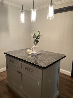 A kitchen with a granite countertop, a white vase with a plant, and three pendant lights. - Modern Home (Mauldin)