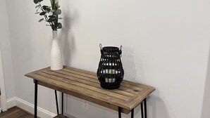 A wooden console table with a woven basket and a vase with greenery. - Modern Home (Mauldin)