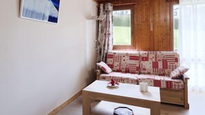 A cozy room with a wooden ceiling, a patterned sofa, a small table, and a window with curtains.