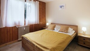 A bedroom with a wooden bed, two bedside tables with lamps, a radiator, and a window with curtains.