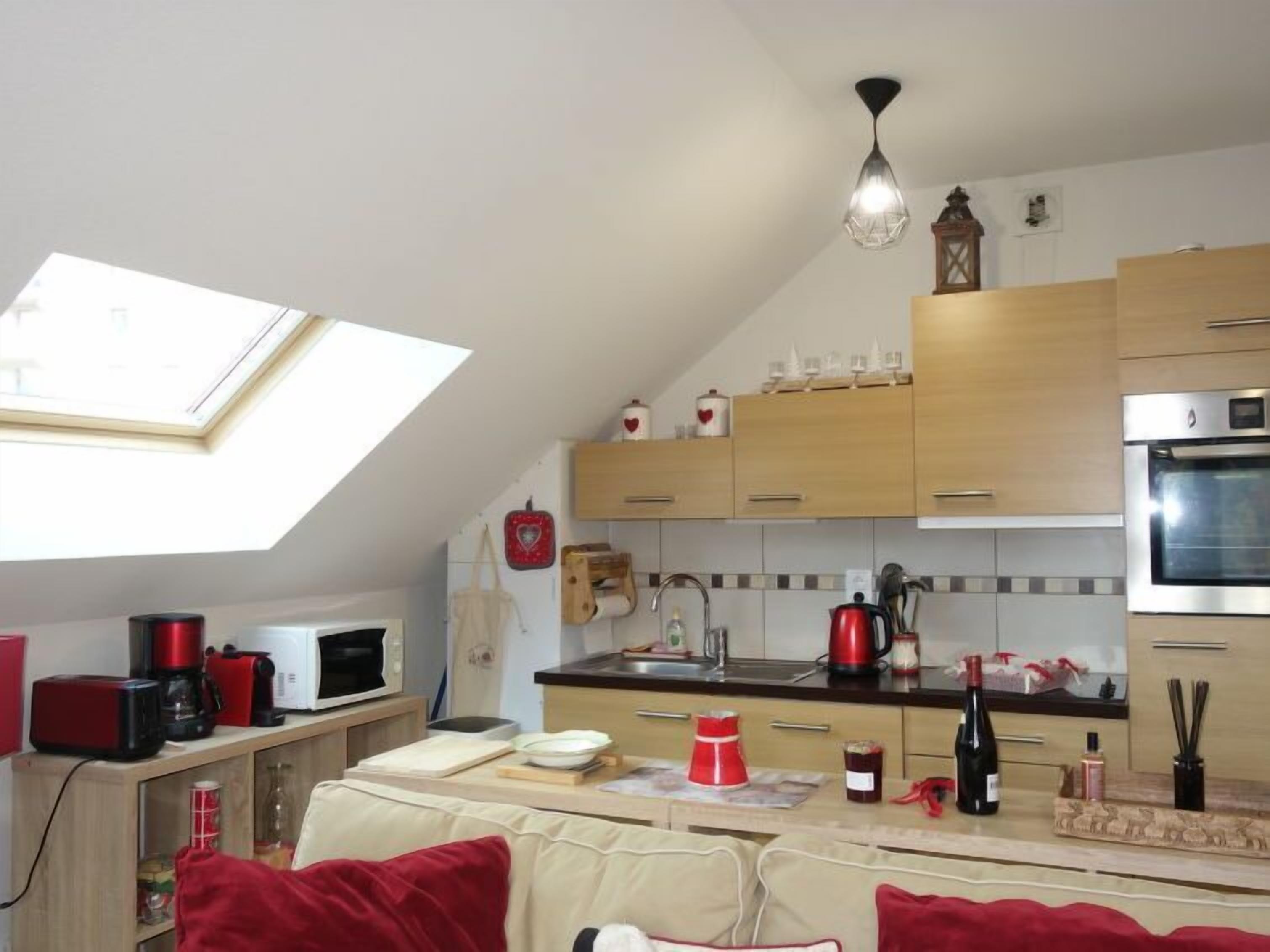A kitchen with wooden cabinets, a skylight, a microwave, a kettle, and a red coffee maker.