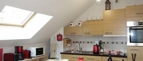 A kitchen with wooden cabinets, a skylight, a microwave, a kettle, and a red coffee maker.