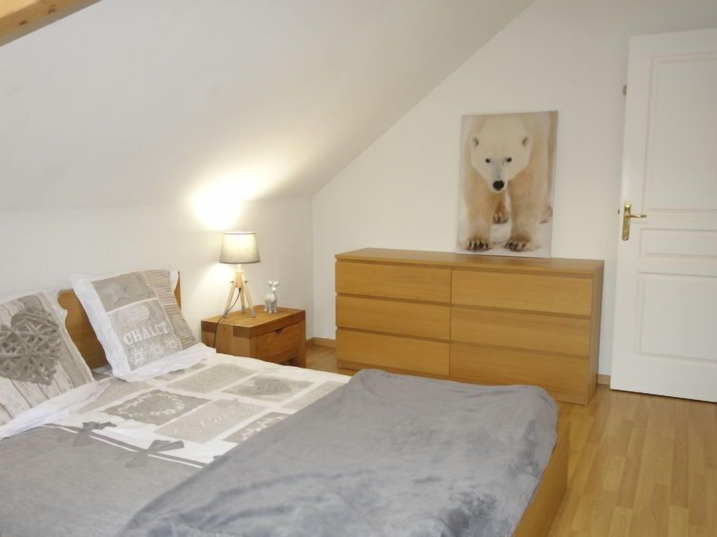 A bedroom with a bed, a nightstand with a lamp, a dresser, and a polar bear painting on the wall.