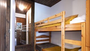 A room with two bunk beds, wooden flooring, and a door leading to another room.