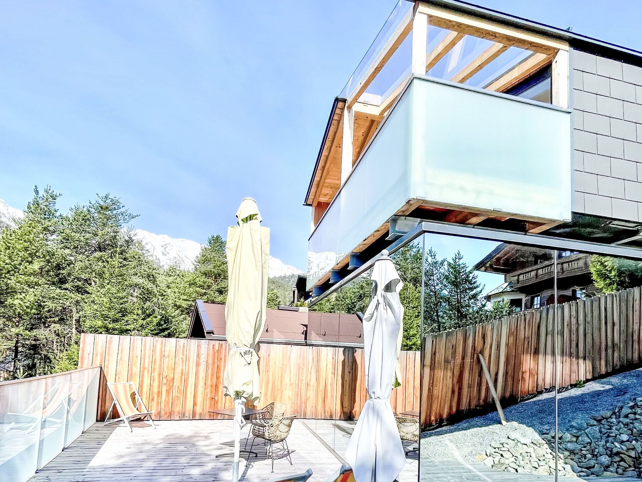 A modern house with a glass balcony, wooden deck, and a view of mountains.