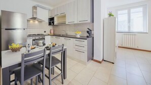 Een moderne keuken met witte kasten, een roestvrijstalen koelkast, een eettafel met stoelen en een raam dat natuurlijk licht binnenlaat.