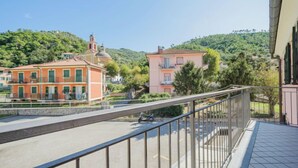 Un balcon doté d’une balustrade en métal, donnant sur une rue bordée d’immeubles, avec une colline en arrière-plan.