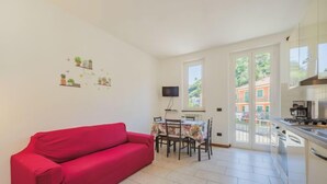 Une cuisine moderne avec un canapé rouge, une table à manger et des chaises. Un téléviseur est fixé au mur et une fenêtre offre une vue sur les bâtiments à l’extérieur.