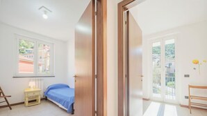 Une chambre à coucher comprenant un lit, une table de chevet, une chaise et une fenêtre donnant sur des immeubles.