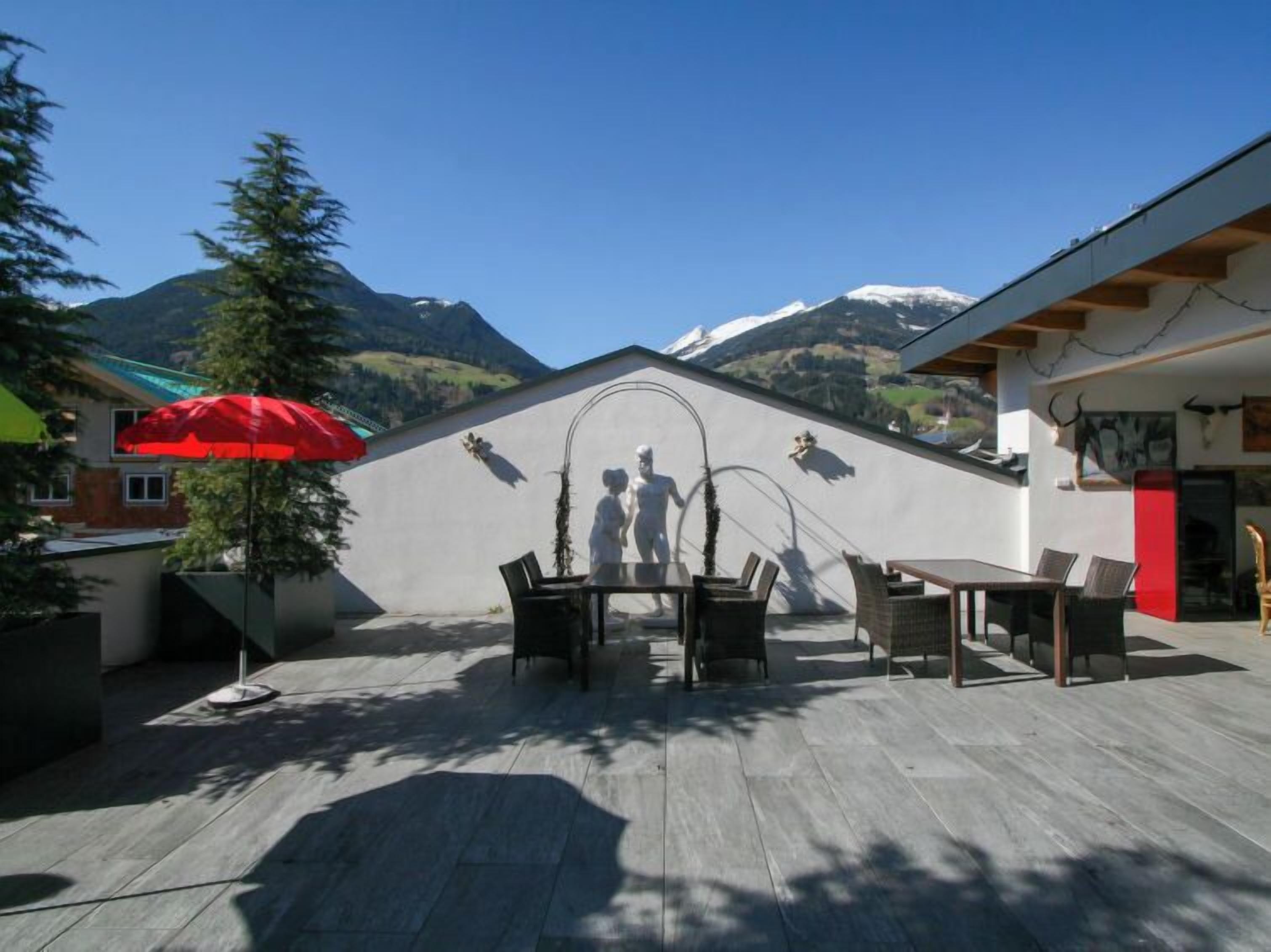 An outdoor patio with a dining table and chairs, a red umbrella, and a mountain view.