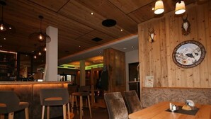 Interno di un ristorante con tavoli e sedie in legno, un'area bar e una parete con una testa di animale appesa.