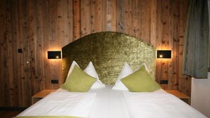 Una stanza con parete in legno, un letto con biancheria bianca e cuscini verdi, e due luci fissate al muro.