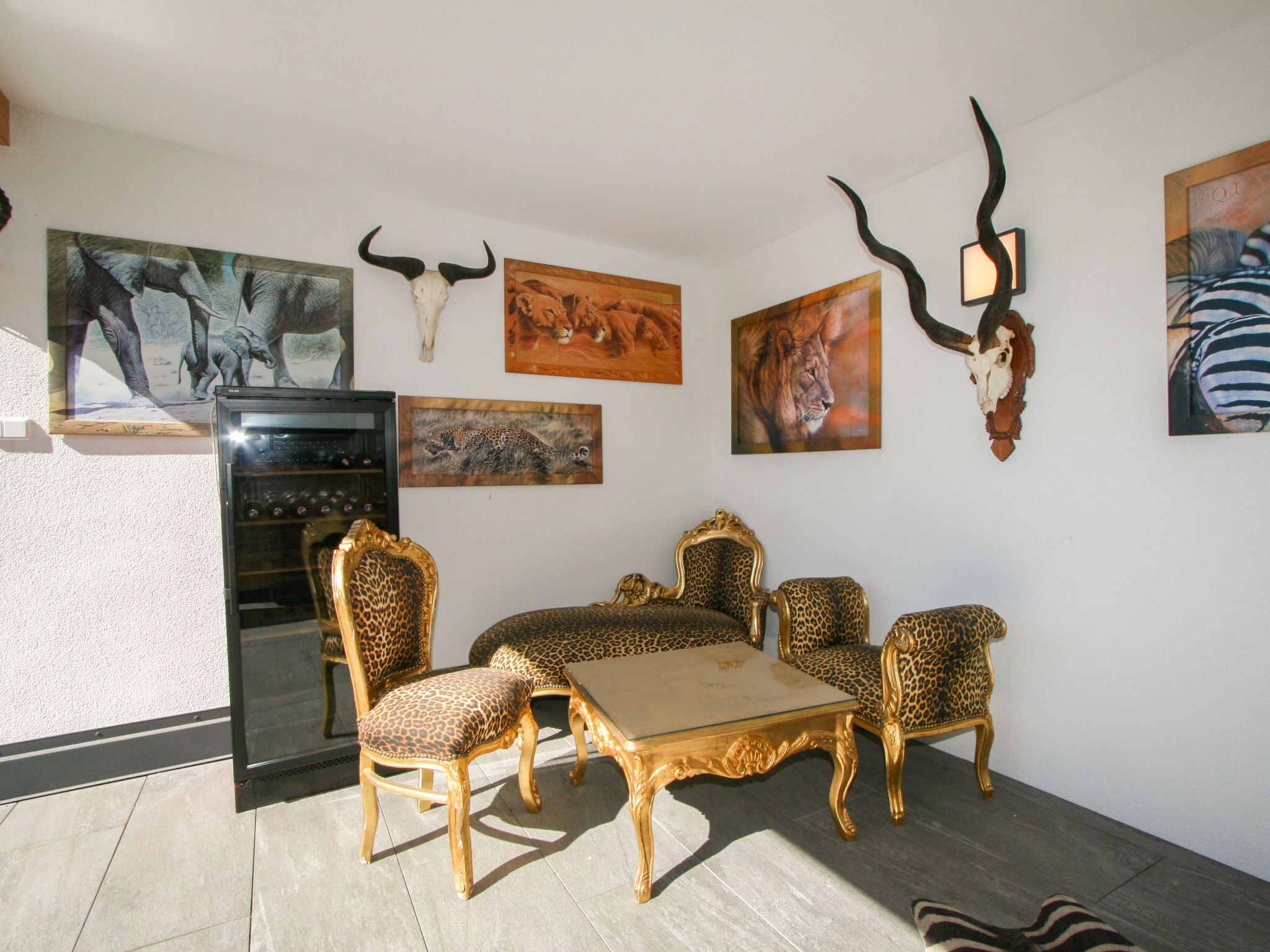 Un coin repas avec une table à plateau en verre et des chaises à motifs léopard, le tout agrémenté d’œuvres d’art sur le thème de la faune et de crânes.